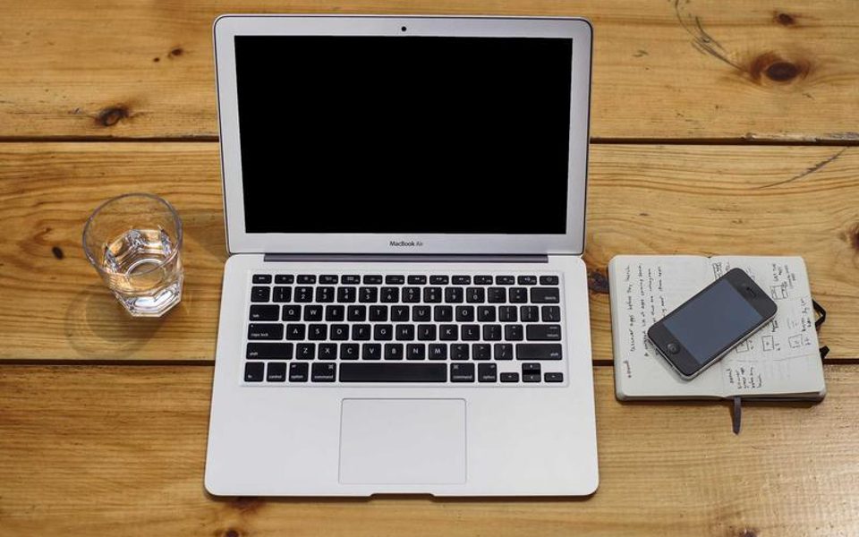 An overhead view of a laptop, phone and notebook